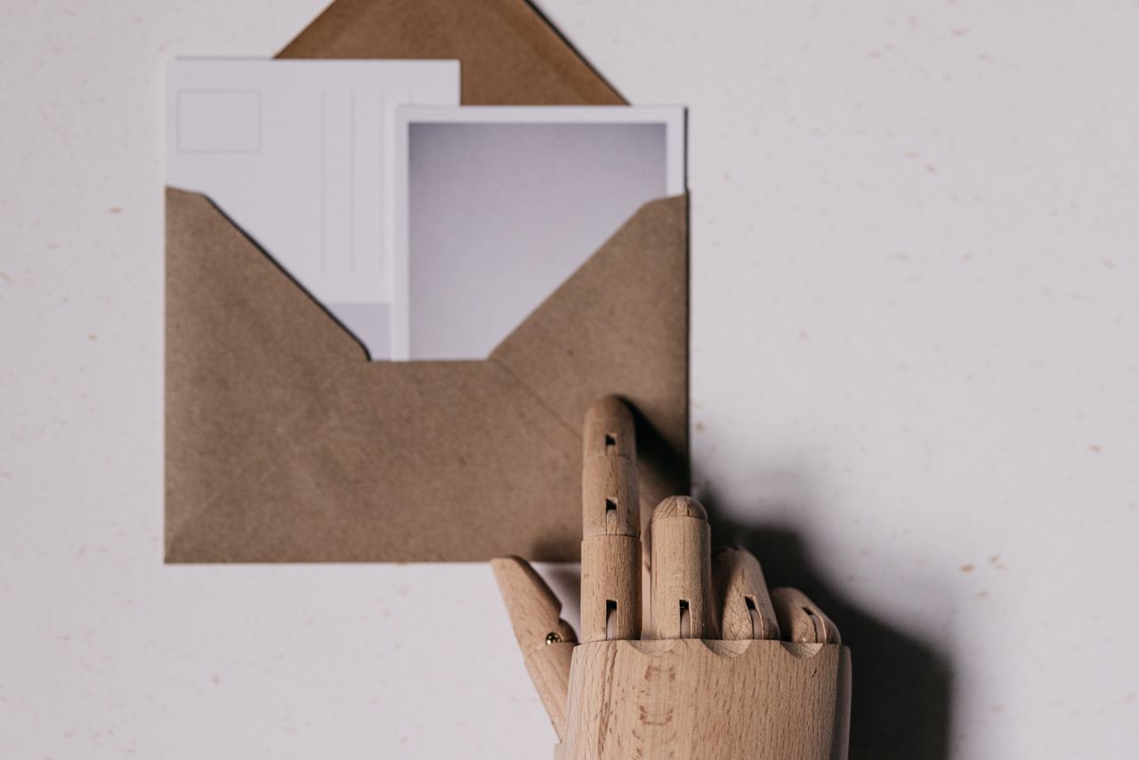 services-01 A wooden mannequin hand holds a brown envelope containing blank postcards.
