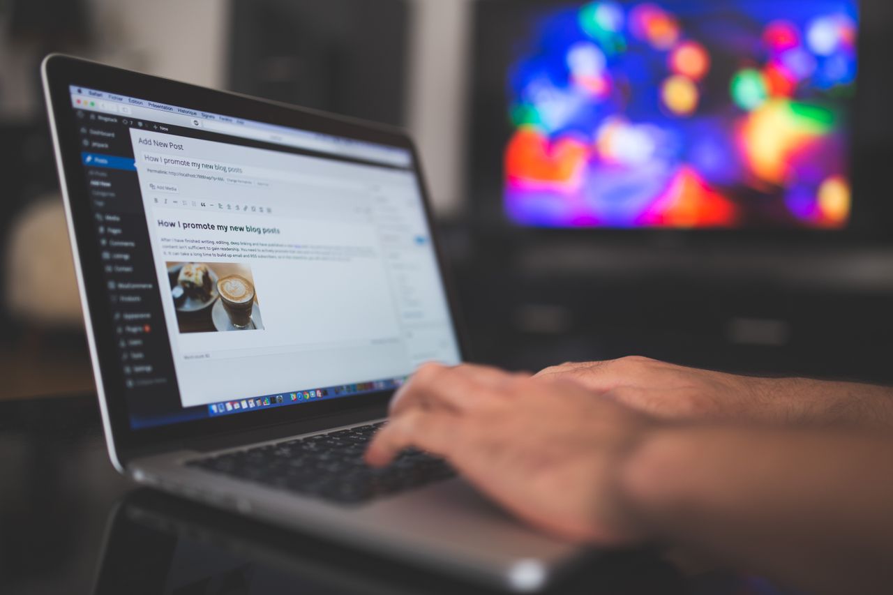 home-hero Hands typing on a laptop with a blog post visible, cozy indoor setting with colorful screen in background.