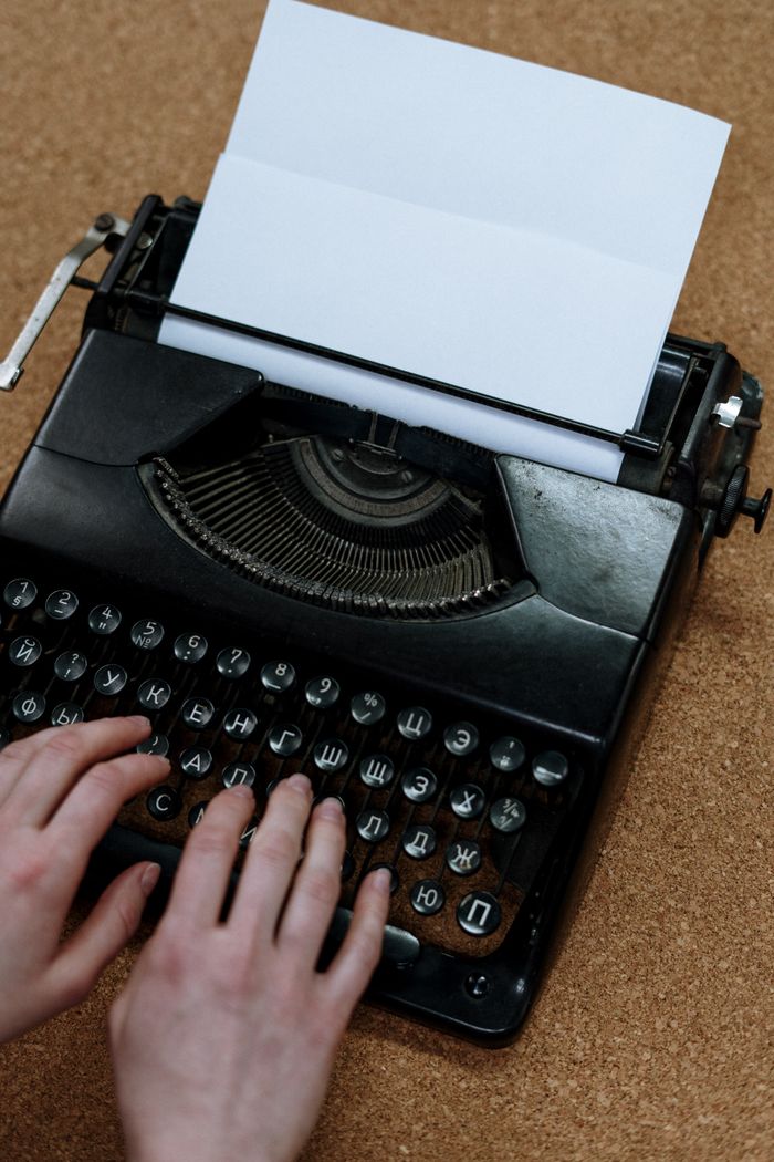 about-bg Close-up of hands typing on a vintage typewriter placed on a corkboard. Classic and retro vibes.