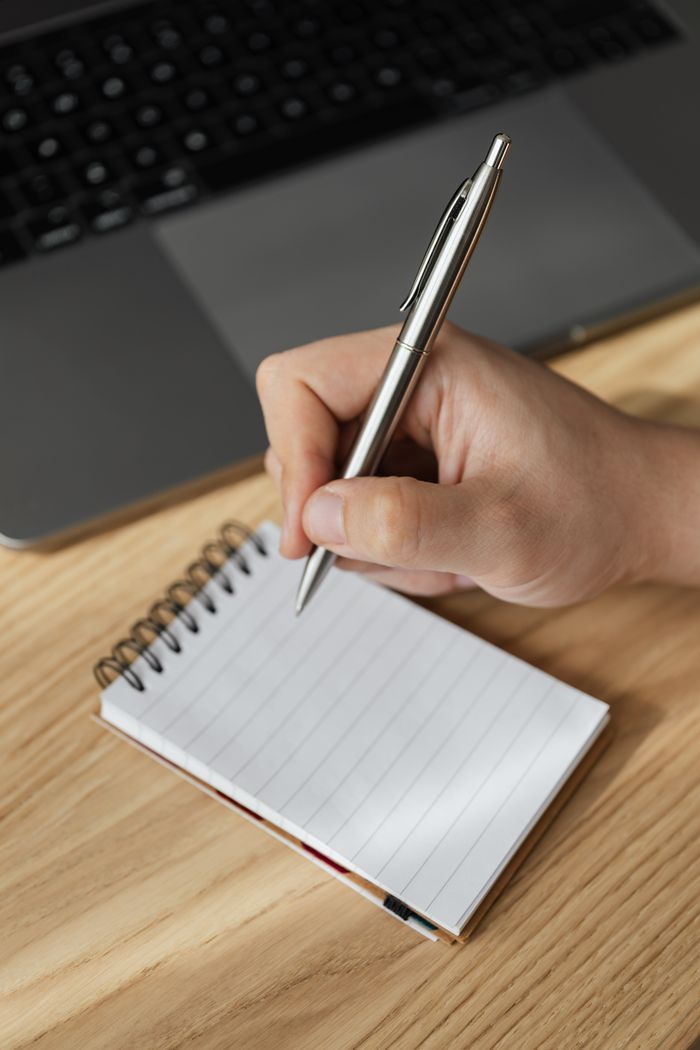 our-story From above of crop anonymous male manager writing in notepad with stylish pen while working at table using laptop