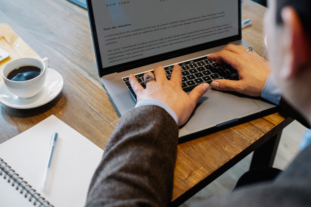 get-in-touch Crop faceless male entrepreneur in formal wear sitting at table with cup of coffee and notebook while working on project in laptop