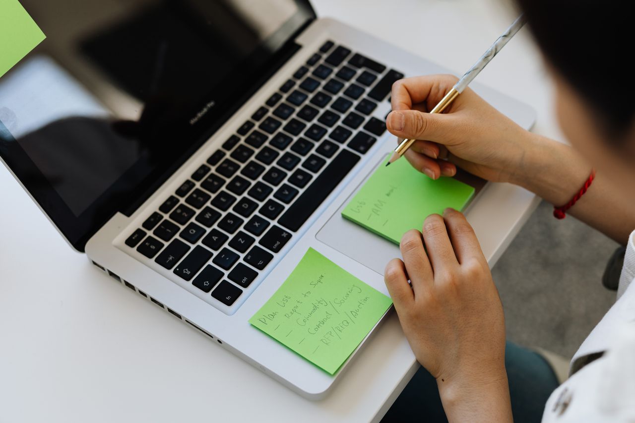 why-choose-us An individual writes notes on green sticky notes placed on a laptop in a work setting.